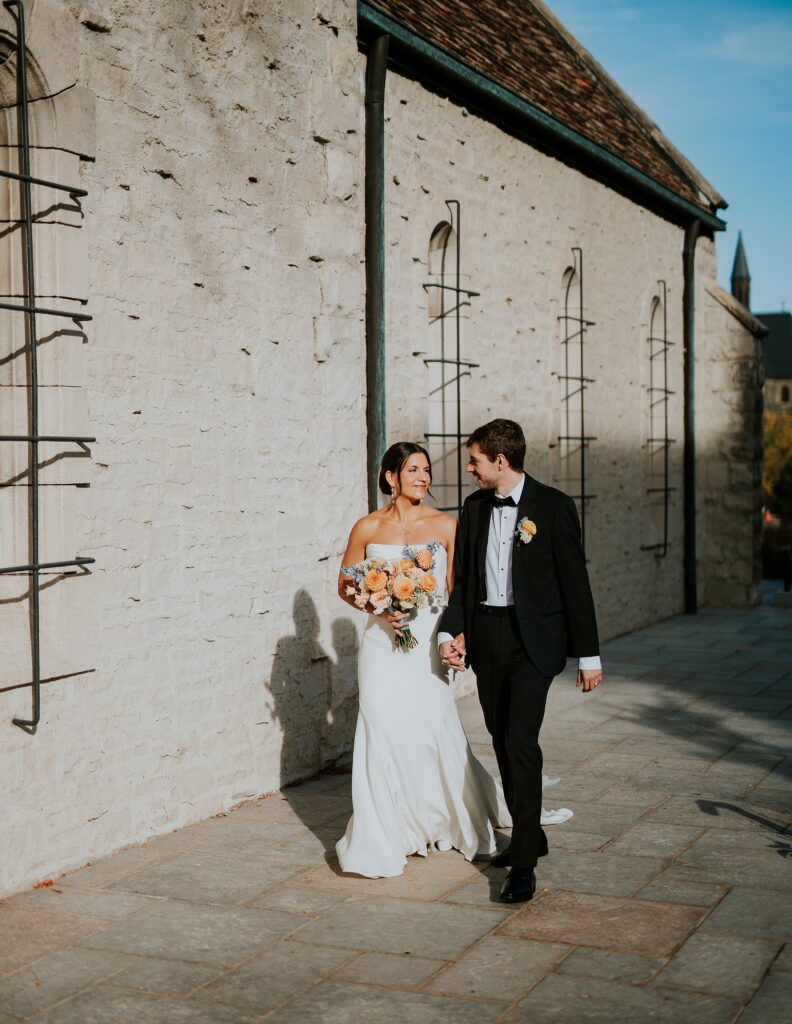 A bride and groom walk along the side of the Saint Joan of Arc chapel in Milwaukee WI